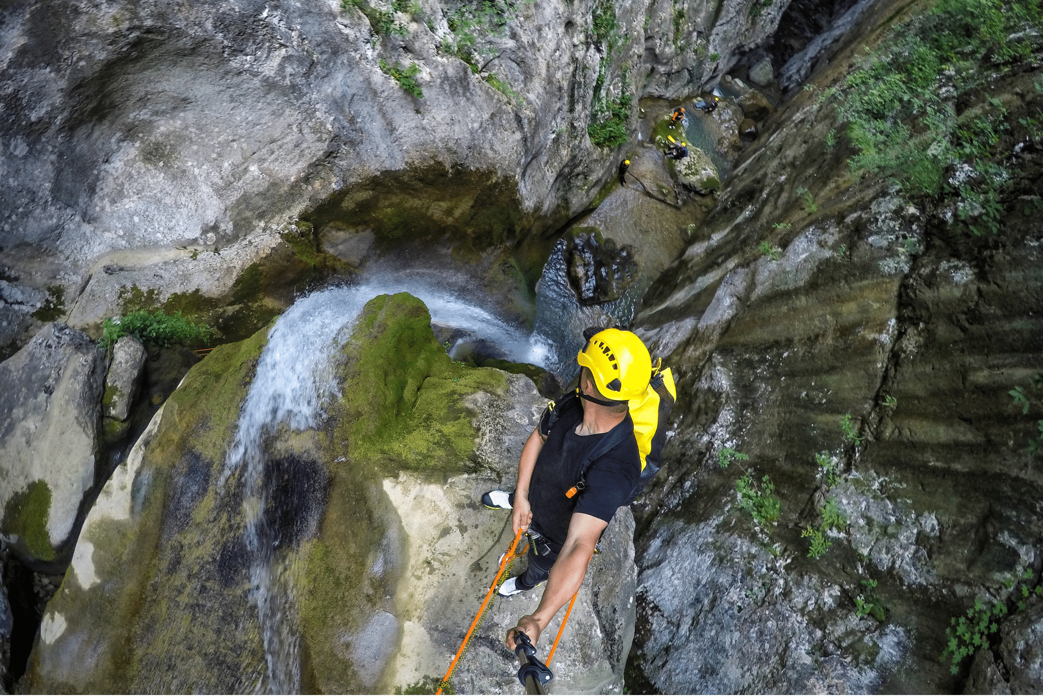 canyoneering member with selfie stick rappelling down the waterfall in the canyon